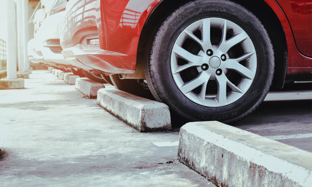 Red car parked up against a concrete wheel stop.