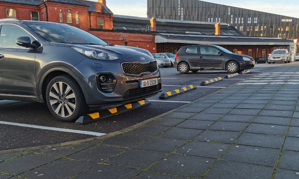 Multiple cars parked in a carpark. Black and yellow wheel stops feature in the foreground.