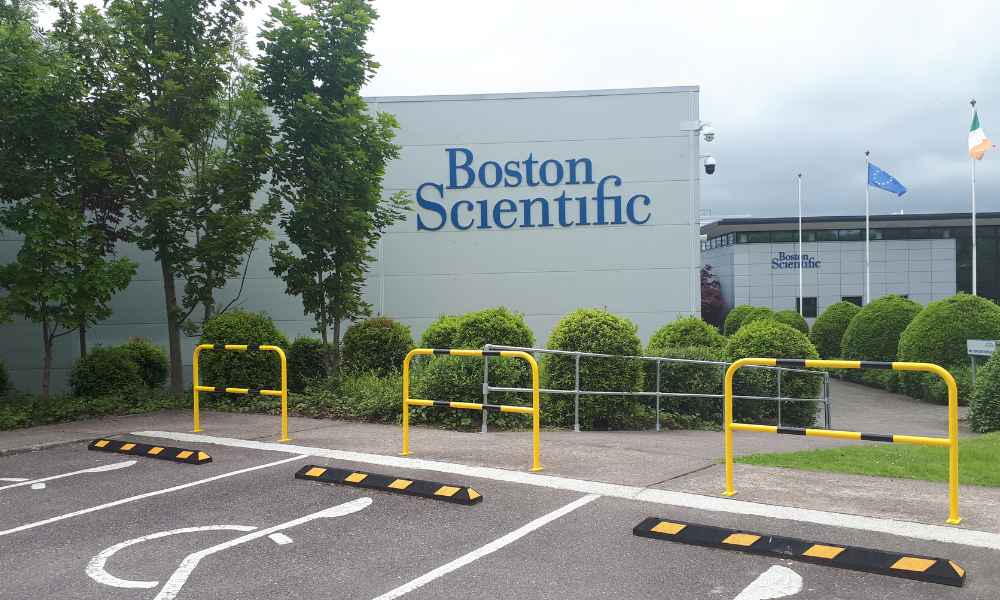 Disabled parking spots in front of an industrial building. Black and yellow wheel stops and hoop guards stop vehicles from mounting the footpath.